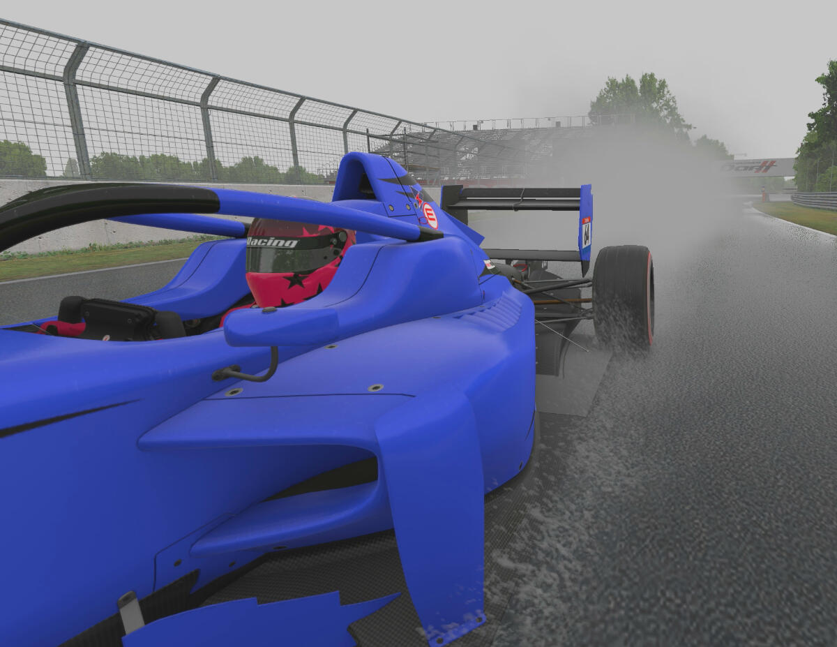 A blue car in a wet Gilles Villeneuve racetrack at Montreal, with a huge plume of spray